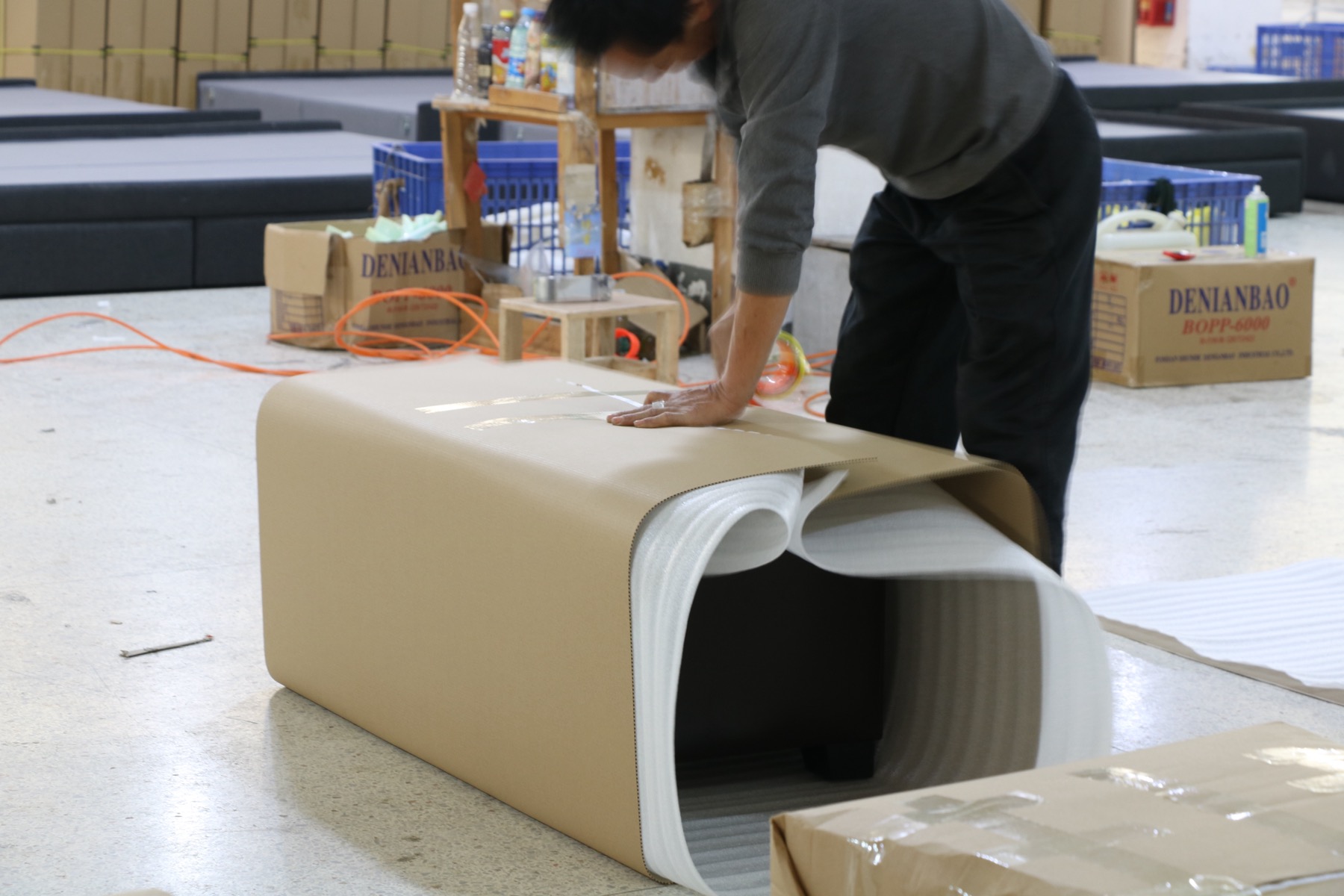 Baotian worker applying protective packaging to upholstered furniture