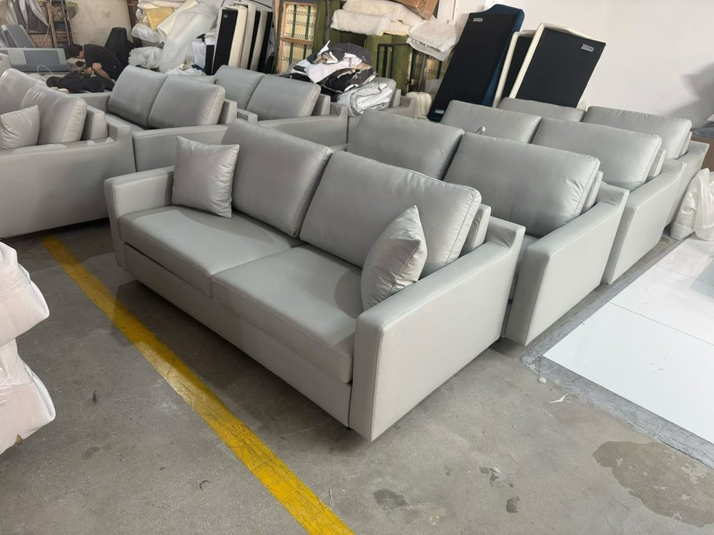 Close view of a light-grey upholstered sofa bed with square arms and loose cushions